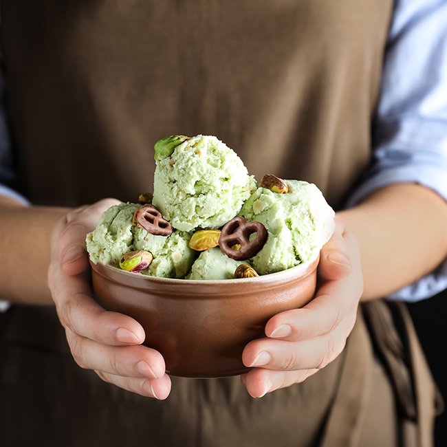 Woman holding bowl full of pistachio ice cream on black background, closeup