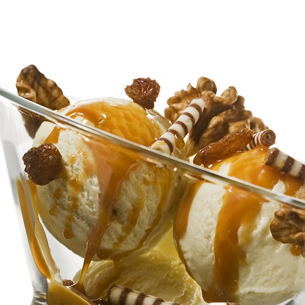 three balls of ice cream with walnuts chocolate rolls raisins and caramel topping in glass bowl isolated on white